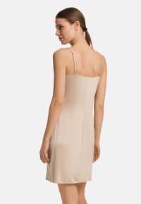 Vestido de satén en beige con tirantes finos ajustables, que presenta una silueta entallada y un diseño sin costuras, con una textura suave y sin patrones visibles.