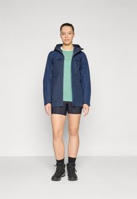 Marint vattentålig jacka, grön skjorta, svarta shorts och slitstarka svarta kängor. Har en huva och dragkedjefickor. Enkelt och funktionellt design.