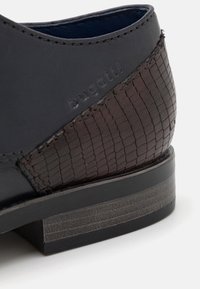 Kožená bota s tmavošedým svrškem a texturovaným hnědým tkaným akcentem. Má nízký černý podpatek s jemným dřevěným vzorem.