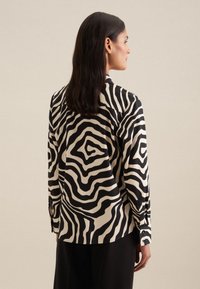 Camicia a maniche lunghe in tessuto leggero con un motivo a zebra ondulato bianco e nero, colletto a punta e polsini con bottoni.