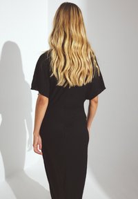 Sort maxikjole med korte, brede ærmer og en tekstureret finish. Silhuetten er tætsiddende og smalner ind ved taljen og hofterne.