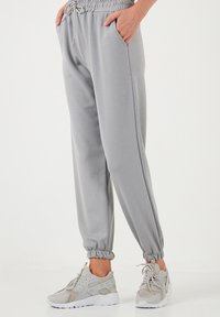 Helle graue Jogginghosen mit einem elastischen Bund, seitlichen Taschen und gerafften Bündchen, kombiniert mit hellgrauen Sneakern. Glattes, lässiges Material.