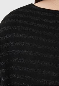 Material tricotat negru cu dungi metalice orizontale. Textura pare netedă, cu un luciu subtil în liniile de accent. Decolteu rotund.