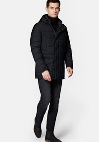 Czarna ocieplana parka z kapturem, z poziomym pikowaniem, dwiema przednimi kieszeniami i zamkiem błyskawicznym. Noszona na czarnym golfie.