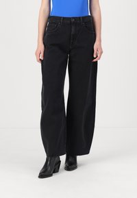 Jeans neri a gamba larga realizzati in denim con vita alta, tasche frontali e orlo grezzo. Indossati con stivaletti neri con tacco.