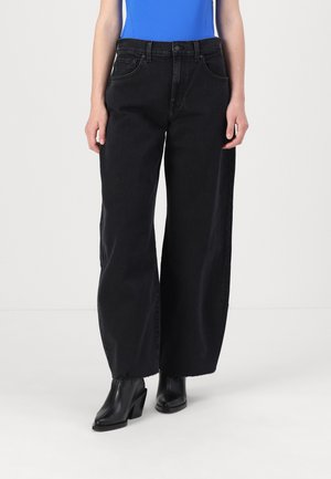 Jeans large noirs en denim avec taille haute, poches avant et ourlet brut. Portés avec des bottines à talons noires.