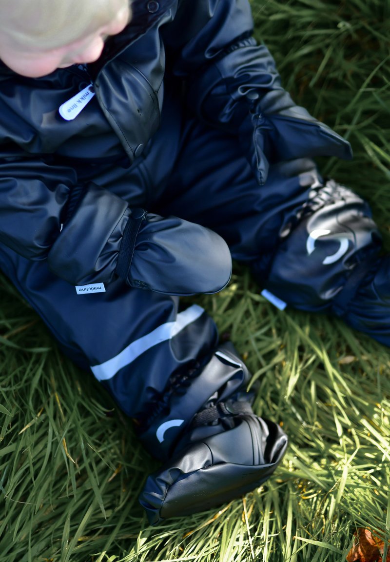 Crni vodootporni skijaški kombinezon s elastičnim manžetama te integriranim rukavicama i čarapama. Reflektirajuće pruge ističu noge; mekana tekstura, punjeni dizajn.