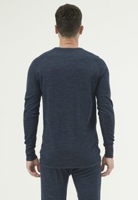Laatikosalla pitkähiha beige ykköspaita, jossa on teksturoitu kangas, pyöreät pääntiellä ja tiukka muotoilu. Ominaisuuksiin kuuluvat ribbireunat ja hieman kaareva helma.