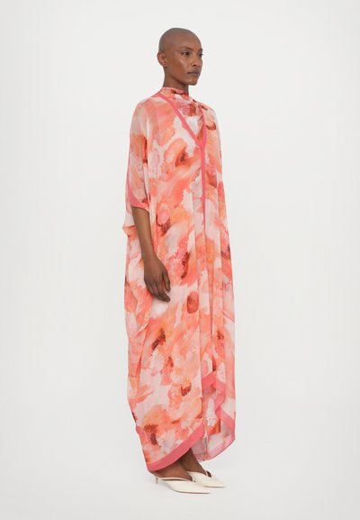 Kaftan fluid, floral în nuanțe de roz, cu guler înalt, material transparent și margine contrastantă. Purtați cu pantofi albi cu toc mic.