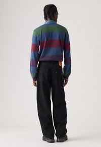 Camicia a maniche lunghe a righe nei colori blu, verde e bordeaux; abbinata a pantaloni ampi neri. Presenta un colletto e un'etichetta della vita visibile.