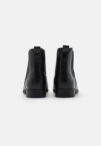Bottines en cuir noir avec panneaux latéraux élastiques, bout arrondi et petits talons empilés. Texture lisse avec des détails de couture contrastants.