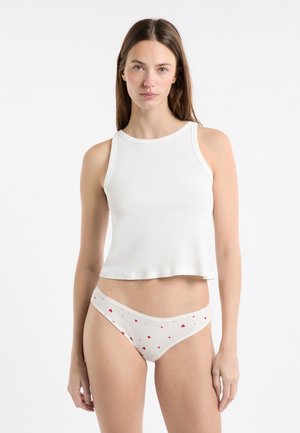 Top corto bianco in tessuto morbido con scollo rotondo, abbinato a biancheria intima crema con motivo di piccoli cuori rossi.