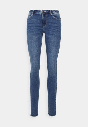 Jeans skinny em denim azul escuro com um design ajustado, estilo de cinco bolsos e detalhes desfiados nas bainhas das pernas. As costuras contrastam com o tecido.