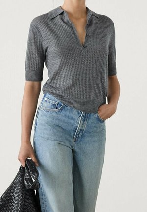 Osoba ubrana w szary, krótki sweter typu polo włożony do jasnoniebieskich, wysokich dżinsów, trzymająca czarną plecioną torbę w lewej ręce.