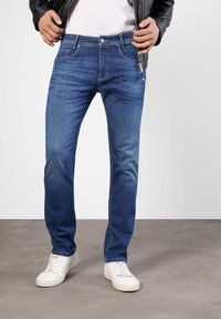 Blue denim jeans with a straight leg design, featuring contrasting stitching and front pockets. Paired with white sneakers.