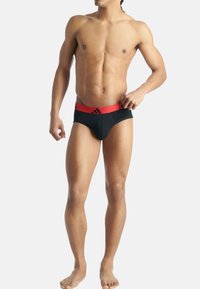 Svart simbyxa med en röd midja som har tre svarta ränder. Tyget verkar slätt och sitter åtsittande mot kroppen.