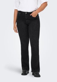 Melnas, taisnas kājas džinsi no šūbēta džinsa, ar izkaisītiem sudraba rotājumiem un priekšējām kabatām. Valkāti kopā ar vaļīgu baltu kreklu.