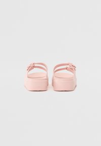 Rosa sandaler med en slät, glansig yta. Har tunna remmar och blommiga dekorationsdetaljer. Tjock, texturerad sula för bra grepp.