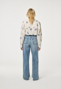 Witte button-up shirt met blauwe patronen, en lichtblauwe, wijde denim jeans met een hoge taille en achterzakken.