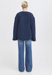 Un pull en polaire oversized bleu marine avec une surface texturée, un col rond et de larges manches, associé à un jean bleu clair à jambes larges.