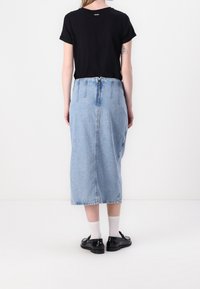 Svart t-shirt med kort ärm och rund halsringning, kombinerad med en ljusblå denim midi-kjol med dragkedja i mitten bak och fransad nederkant.