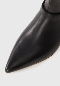 Stivale in pelle nera con punta a punta e superficie liscia. Presenta un'apertura alla caviglia stretta e un design minimalista.