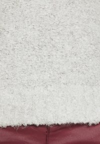 Gros plan sur un tissu bouclé blanc texturé au-dessus d'un cuir bordeaux lisse avec des coutures visibles.