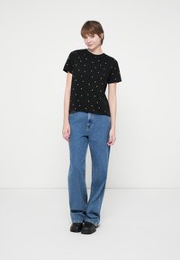 Črna majica s kratkimi rokavi, na kateri so majhni rumeni srčki, v kombinaciji z svetlo modrimi naravnost krojenimi jeans hlačami in črnimi čevlji. Enostaven dizajn.