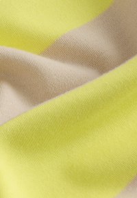 Textílie v jasne žltej a svetlobéžovej farbe, s hladkou, mäkkou textúrou, viditeľnými vzormi pletenia a farebnými blokmi.