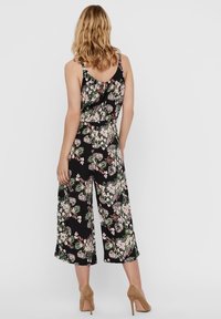 Jumpsuit floreale con sfondo nero, caratterizzato da una vestibilità rilassata, gambe ampie e scollo a barca. Accentuato da motivi rosa e verdi.