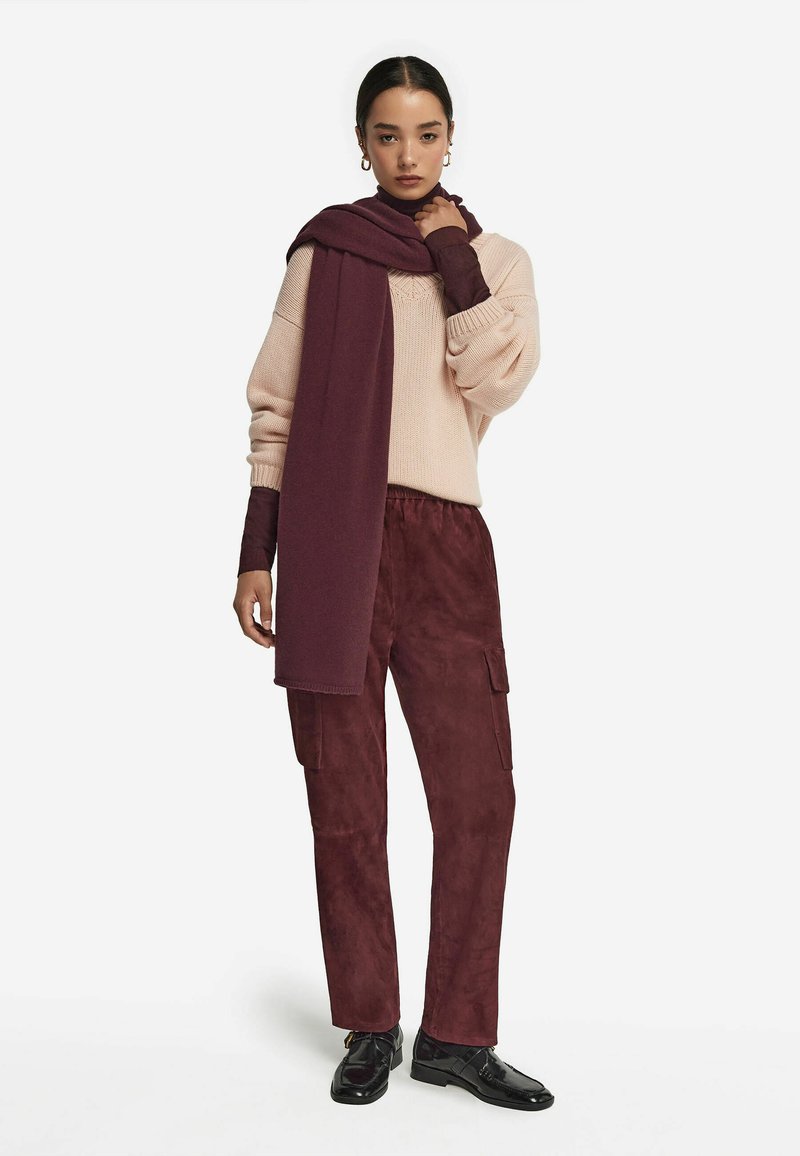 Lyserød strikket sweater med en løs pasform, parret med bordeauxfarvede ruskinds cargo bukser. Et matchende bordeauxfarvet tørklæde hænger om halsen og fremhæver looket.