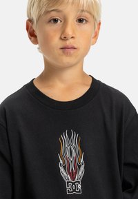 Zwarte katoenen t-shirt met een vlamontwerp in wit, rood en oranje; een logo in het midden onder de afbeelding. Ronde hals en korte mouwen.