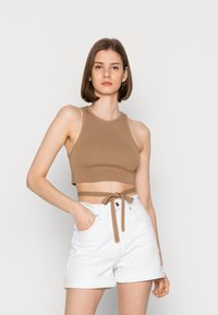 Top cropped castanho com nervuras, com pescoço halter e laço lateral, combinado com calções brancos de bainha dobrada, com bolsos frontais e fecho de botão.