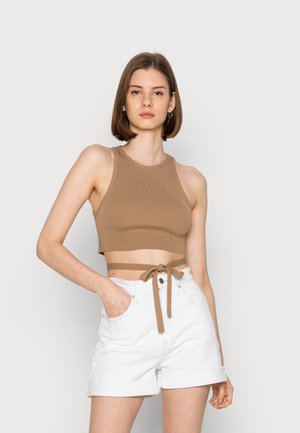 Top cropped castanho com nervuras, com pescoço halter e laço lateral, combinado com calções brancos de bainha dobrada, com bolsos frontais e fecho de botão.