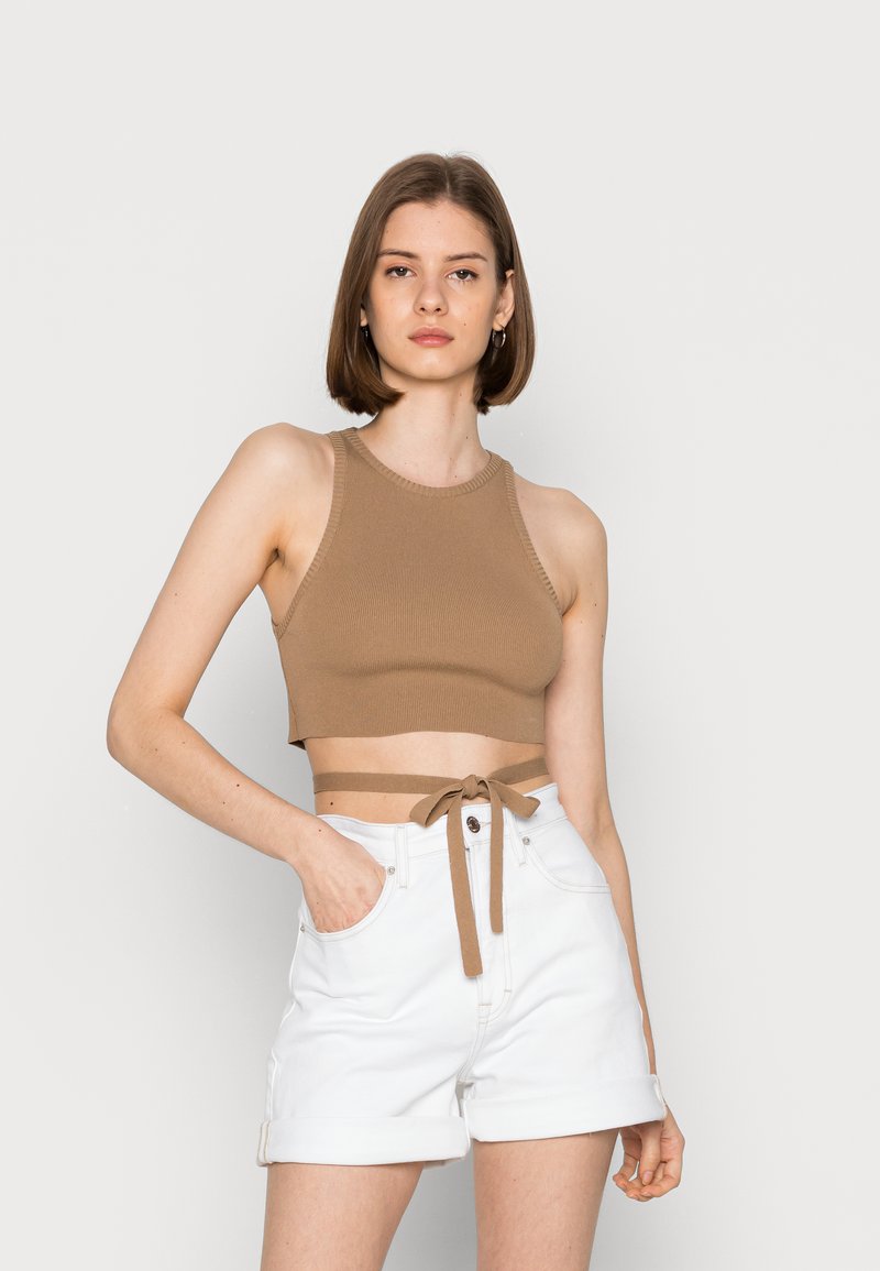 Top cropped castanho com nervuras, com pescoço halter e laço lateral, combinado com calções brancos de bainha dobrada, com bolsos frontais e fecho de botão.