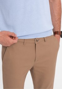 Beżowe chinosy o gładkiej fakturze, z zapięciem na guzik i szlufkami na pasek. Noszone z jasnoniebieskim, swetrem z dzianiny.