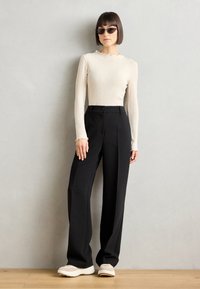 Beige ribbet langermet topp med bølgekant i halsen, kombinert med høyt liv svarte vide bukser og lyse chunkysneakers.