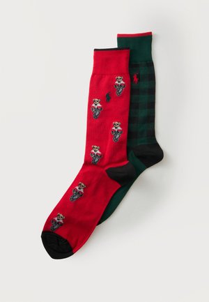 Une chaussette rouge avec de petites figures de chiens portant des vestes et une chaussette à carreaux noire et verte avec un logo cheval rouge.