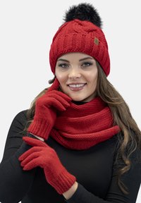 Cappello lavorato a maglia rosso con un pompon nero, guanti coordinati e una sciarpa spessa. Presenta motivi a coste e testurizzati, adatti per l'inverno.