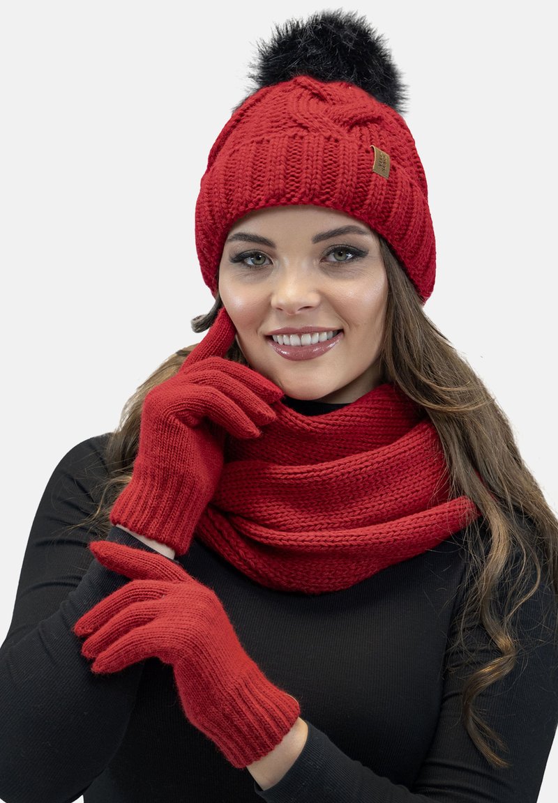 Cappello lavorato a maglia rosso con un pompon nero, guanti coordinati e una sciarpa spessa. Presenta motivi a coste e testurizzati, adatti per l'inverno.