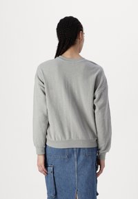 Sudadera gris de corte relajado, con puños y dobladillo acanalados, combinada con una falda de mezclilla que presenta bolsillos y una abertura alta en el muslo.