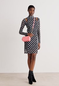 Vestito nero a pois con maniche lunghe e dettagli a taglio; abbinato a una borsa a tracolla rosa e stivaletti neri alla caviglia. Tessuto dalla trama liscia.