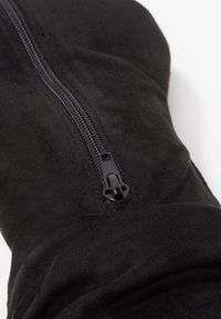 Botín de microfibra negra con una textura suave, que presenta una cremallera lateral prominente hecha de metal negro brillante.