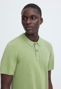 Polo vert clair en maille texturée, manches courtes, trois boutons assortis, et col classique. Coupe lisse et décontractée.