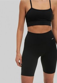 Set atletico nero composto da un crop top testurizzato e pantaloni corti a vita alta. Il tessuto è liscio con una vestibilità aderente, accentuato da un branding minimale.
