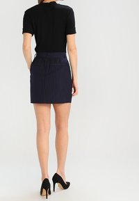 Černá košile s krátkým rukávem v kombinaci s námořnickou mini sukní s proužky; hladká tkanina; přiléhavý střih; obuto s černými vysokými podpatky.