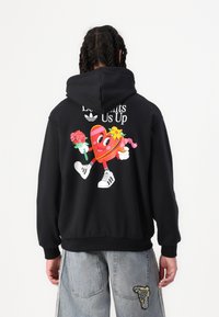 Black hoodie featuring a colorful cartoon heart graphic on the back, holding flowers, with "Let It Lights Us Up" text and Adidas logo.