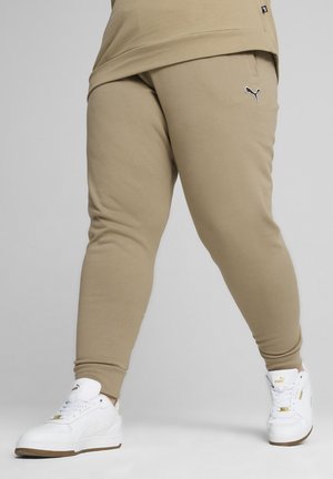 Pantaloni jogger beige con gambe affusolate, vita elastica e un piccolo logo Puma nero. Abbinati a sneakers bianche. Materiale in cotone morbido.
