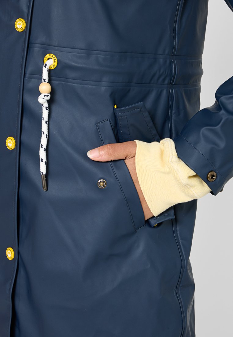 Cappotto impermeabile navy con accenti gialli, bottoni a pressione e cordino texture. Presenta una tasca laterale e un polsino interno a contrasto.