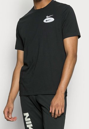 T-shirt en coton noir à manches courtes, arborant un logo Nike blanc sur la poitrine. Le tissu semble lisse avec une coupe classique.